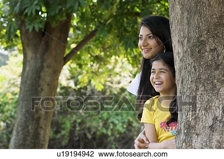 Stock Image - Mother and daughter standing beside a tree . Fotosearch