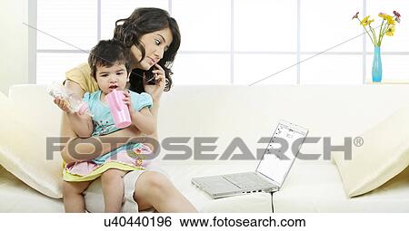 Stock Photograph - Mother holding her child while talking on the phone . Fotosearch