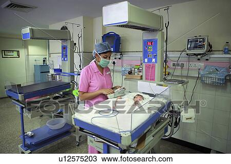 Stock Image - Nurse tending to newborn baby in hospital nursery . Fotosearch