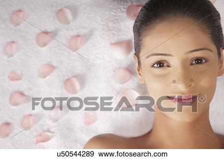 Stock Photo - Portrait of a beautiful young woman lying on massage table with petals . Fotosearch