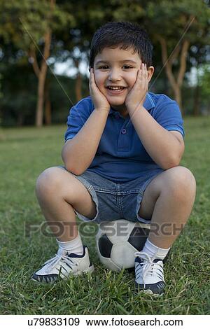 Stock Photo - Portrait of a young boy sitting on a football. Fotosearch
