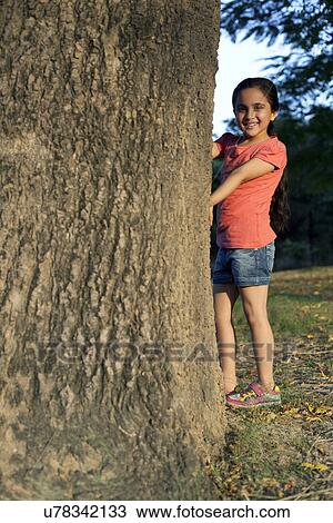Stock Image - Portrait of a young girl standing beside a tree. Fotosearch