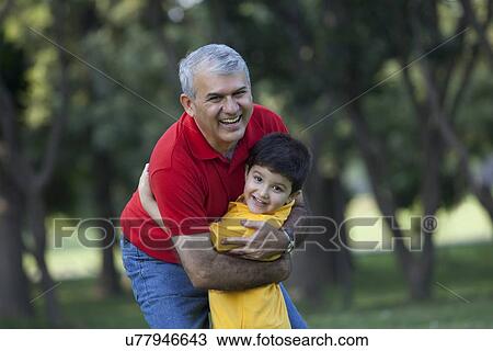 Stock Image - Portrait of grandfather and grandson hugging in a park. Fotosearch