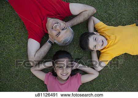 Stock Image - Portrait of grandfather and grandchildren lying in the grass. Fotosearch