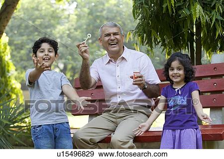 Stock Photo - Portrait of grandfather with grandkids blowing bubbles in park. Fotosearch
