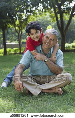Stock Image - Portrait of grandson hugging grandfather in park. Fotosearch