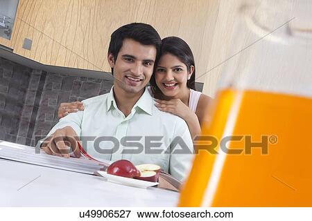 Portrait of happy couple with apple and catalogues in kitchen View Large Photo Image Stock Photo - Portrait of happy couple with apple and catalogues in kitchen. Fotosearch