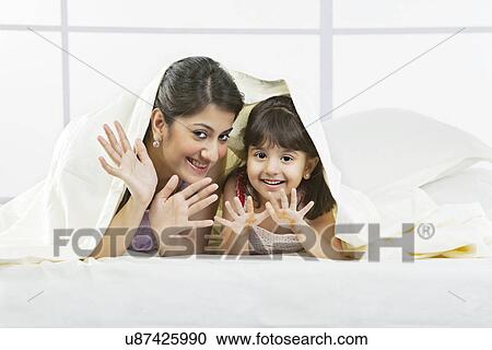Stock Image - Portrait of mother and daughter under a bed sheet . Fotosearch