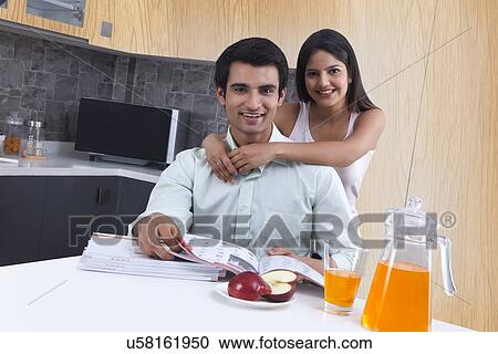 Portrait of woman embracing man from behind at kitchen island View Large Photo Image Stock Image - Portrait of woman embracing man from behind at kitchen island. Fotosearch