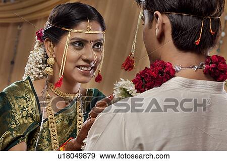 Stock Photo - Pretty young bride smiling while performing garland ceremony . Fotosearch
