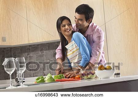 Stock Image - Romantic couple cutting vegetables together in kitchen. Fotosearch