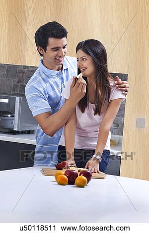 Stock Image - Romantic man feeding apple to woman in kitchen. Fotosearch