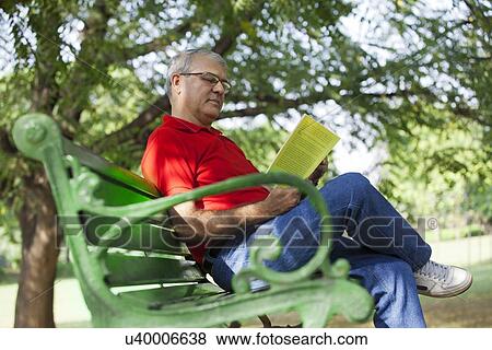 Stock Photo - Senior man reading a book in a park. Fotosearch