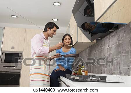 Stock Image - Smiling couple preparing food in kitchen. Fotosearch