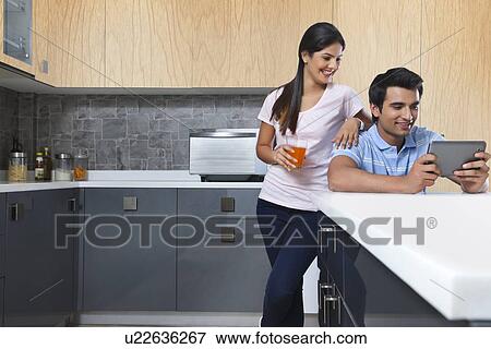 Stock Photo - Smiling couple using digital tablet in kitchen. Fotosearch