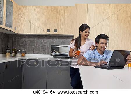 Smiling couple using laptop in kitchen View Large Photo Image Picture - Smiling couple using laptop in kitchen. Fotosearch