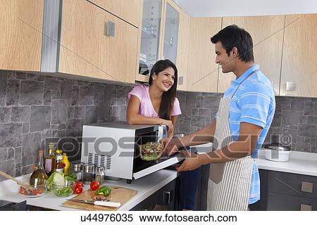 Stock Photography - Smiling woman looking at man cooking in kitchen. Fotosearch