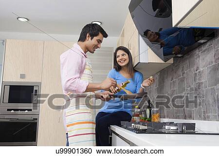 Stock Image - Smiling young couple preparing food in kitchen. Fotosearch