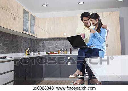 Smiling young couple using laptop in kitchen View Large Photo Image Stock Photo - Smiling young couple using laptop in kitchen. Fotosearch