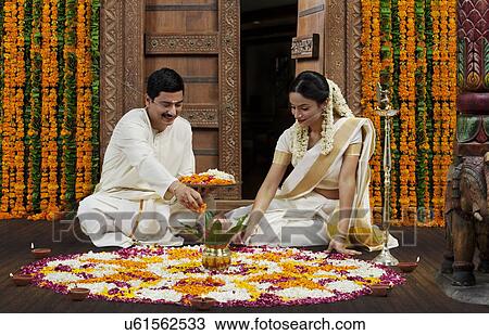 Stock Image - South Indian couple making a flower rangoli . Fotosearch