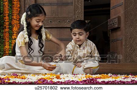 Stock Image - South Indian girl helping her brother with a rangoli . Fotosearch