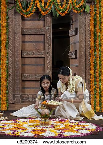 Stock Image - South Indian woman helping her daughter with a rangoli . Fotosearch