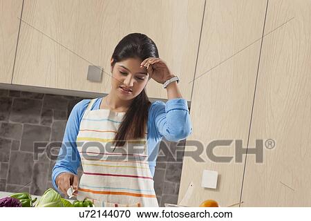 Stock Image - Tired young woman preparing food in kitchen. Fotosearch