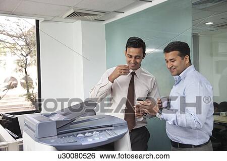 Stock Photograph - Two male executives looking at an sms on a mobile phone. Fotosearch