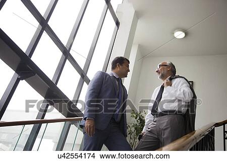 Picture - Two male executives talking on a staircase. Fotosearch