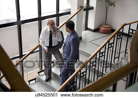 Two male executives talking on a staircase View Large Photo Image Stock Image - Two male executives talking on a staircase. Fotosearch