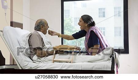Stock Image - Wife feeding her husband in a hospital . Fotosearch