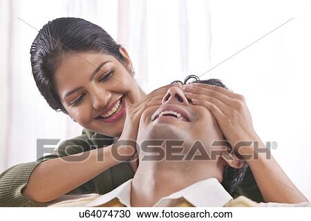 Stock Image - Woman covering mans eyes with her hands. Fotosearch
