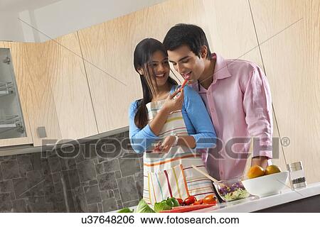 Woman feeding carrot to man in kitchen View Large Photo Image Stock Photograph - Woman feeding carrot to man in kitchen. Fotosearch
