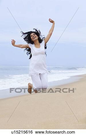 Stock Photograph - Woman jumping in the air at a beach . Fotosearch