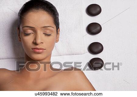 Stock Image - Woman lying on massage table with pebble stones on side . Fotosearch