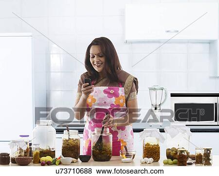 Stock Photo - Woman reading an sms while making pickle . Fotosearch