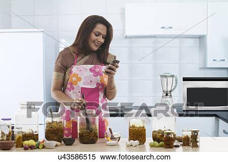 Stock Photography - Woman reading an sms while making pickle . Fotosearch
