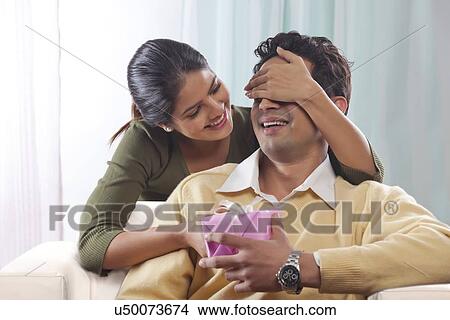Picture - Woman surprising a man with a gift on Valentines Day. Fotosearch