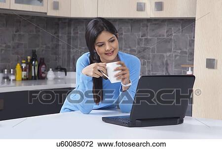 Woman with coffee mug looking at laptop in kitchen View Large Photo Image Stock Image - Woman with coffee mug looking at laptop in kitchen. Fotosearch