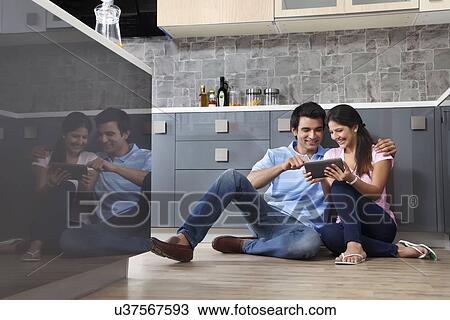 Stock Image - Young couple using digital tablet together in kitchen. Fotosearch
