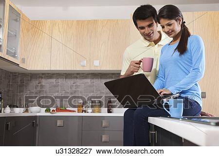 Stock Photo - Young couple using laptop in kitchen. Fotosearch