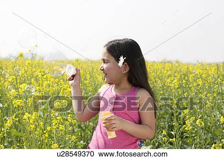 Stock Image - Young girl making bubbles in a field . Fotosearch