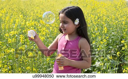 Stock Image - Young girl making bubbles in a field . Fotosearch