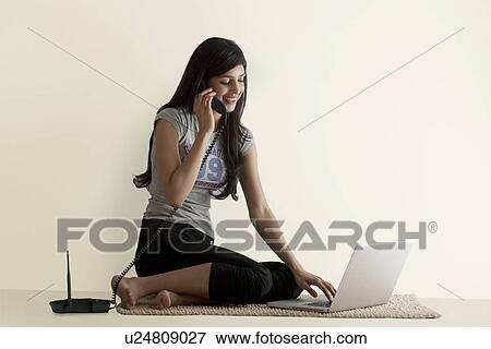 Stock Photo - Young girl with a laptop talking on a phone . Fotosearch