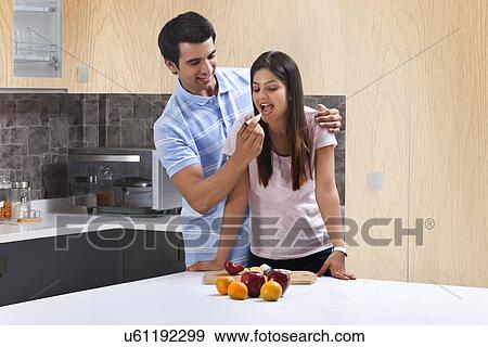 Stock Photo - Young man feeding apple to woman in kitchen. Fotosearch