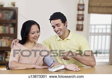 Young man sitting with mother pointing at blood pressure gauge View Large Photo Image Stock Image - Young man sitting with mother pointing at blood pressure gauge . Fotosearch
