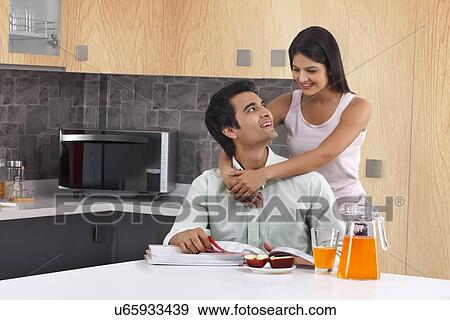 Young woman embracing man from behind in kitchen View Large Photo Image Stock Photo - Young woman embracing man from behind in kitchen. Fotosearch