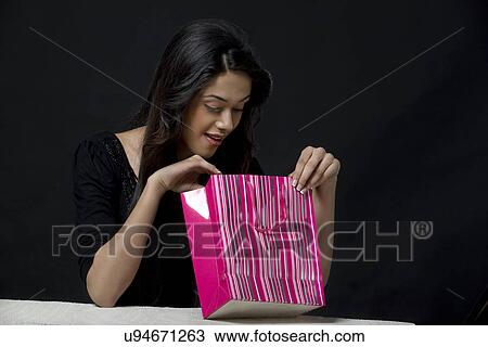 Stock Image - Young woman looking inside a shopping bag . Fotosearch