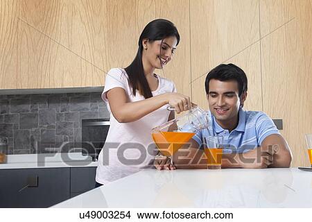 Picture - Young woman pouring juice for man in kitchen. Fotosearch