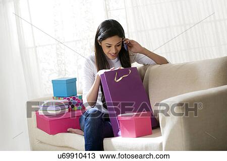 Stock Image - Young woman talking on a mobile phone while looking inside a gift bag . Fotosearch